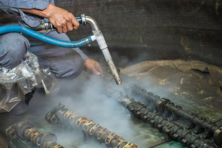 Operatore esegue sabbiatura criogenica su componenti metallici in un'industria a Brescia, utilizzando un dispositivo specializzato per rimuovere contaminanti con basse temperature.