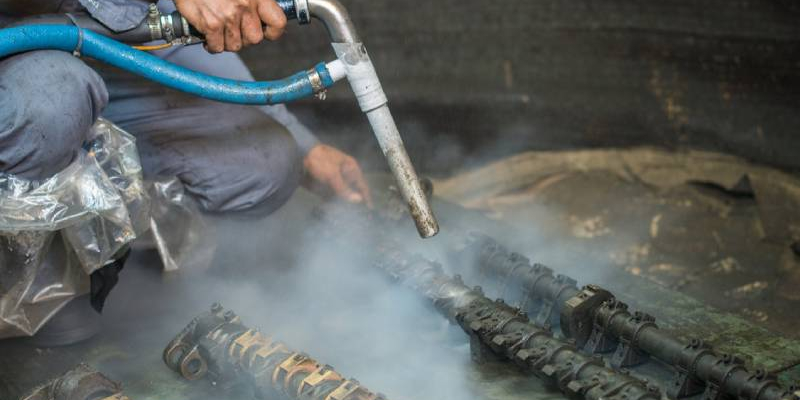 Operatore esegue sabbiatura criogenica su componenti metallici in un'industria a Brescia, utilizzando un dispositivo specializzato per rimuovere contaminanti con basse temperature.