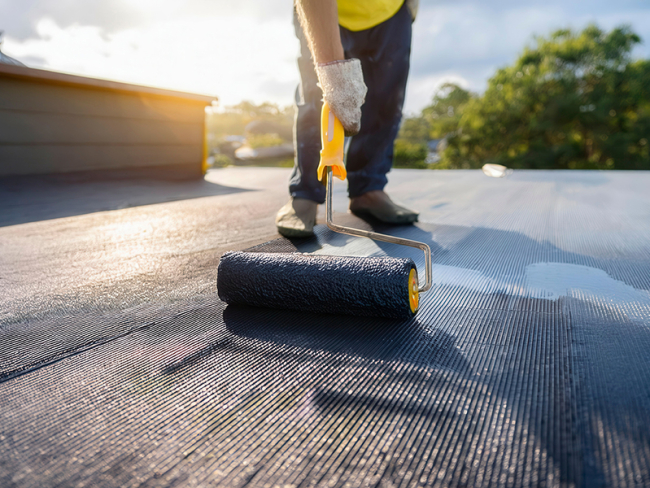 Applicazione professionale di membrane liquide bituminose su un tetto piano a Cremona. La scena mostra un operatore che utilizza un rullo per stendere la membrana impermeabilizzante, con un risultato uniforme e resistente.